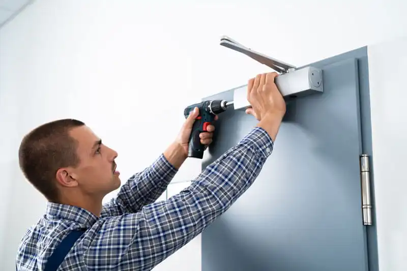 Technician installing a door closer on a gray door with a drill